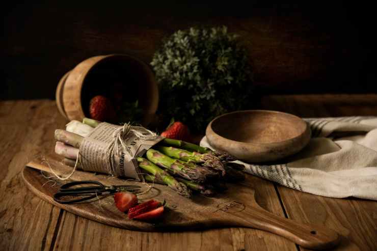 Olika billiga grönsaker som sparris och jordgubbar ligger på en skärbräda i trä
